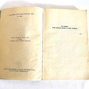 May include: Open vintage book with text: "TO THOSE WHO WOULD BUILD A NEW WORLD." The book's pages are aged, with text from "First Edition, 3,000 Copies, September 1960." Published by The Navajivan Trust in India.
