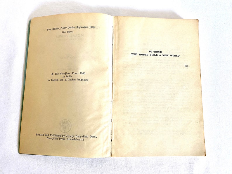 May include: Open vintage book with text: "TO THOSE WHO WOULD BUILD A NEW WORLD." The book's pages are aged, with text from "First Edition, 3,000 Copies, September 1960." Published by The Navajivan Trust in India.