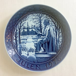 Könnte beinhalten: Ein blauer und weißer Weihnachtsteller mit einer Winterszene, die einen Mann im Mantel und ein Gebäude zeigt. Der Teller trägt den Text "JULEN 1978" und "H.C. ANDERSEN".