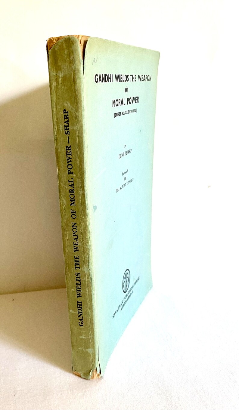 May include: A vintage book titled "Gandhi Wields the Weapon of Moral Power" by Gene Sharp. The book has a light green cover with black text. The spine shows the title and author. The book's edges show signs of wear.