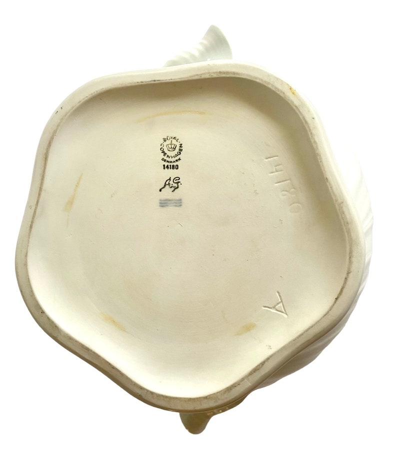 Pu&ograve; includere: Teiera in ceramica bianca con un motivo floreale. La parte inferiore della teiera presenta il logo Royal Copenhagen e il numero 14180.