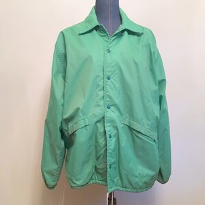 Könnte beinhalten: Eine grüne, leichte Jacke mit Knopfleiste und Kordelzug am Saum.