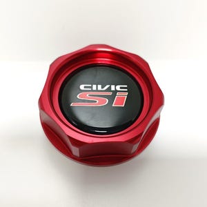 May include: A circular red metal oil cap featuring a black centre insert with the white text CIVIC and the red text Si printed on it. The cap has a scalloped, multi-sided outer edge design and a smooth, polished finish on the metallic surface.