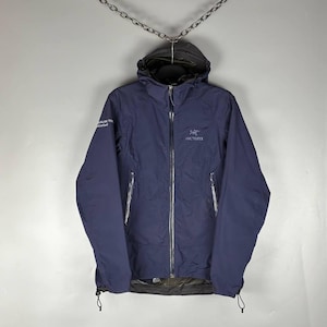May include: A dark navy blue hooded jacket featuring a full-length front zipper, long sleeves, and two zippered side pockets. The Arc'teryx logo is embroidered on the left chest, and white text is printed on the right upper sleeve.