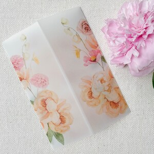 Op de afbeelding: Een witte envelop met een bloemenontwerp met roze en oranje bloemen. De envelop ligt op een wit, getextureerd oppervlak.