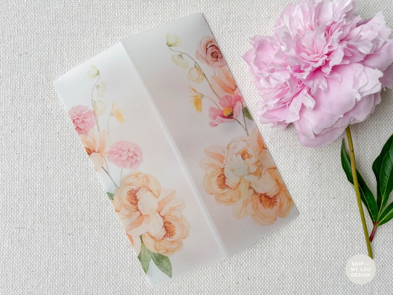 Op de afbeelding: Een witte envelop met een bloemenontwerp met roze en oranje bloemen. De envelop ligt op een wit, getextureerd oppervlak.