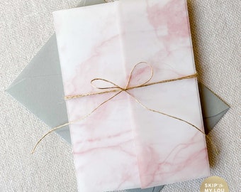 May include: A pink and white marble patterned invitation with a brown twine bow. The invitation is folded in half and is sitting on a gray envelope.