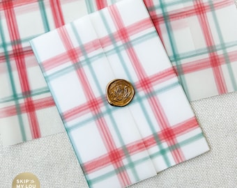 May include: A white envelope with a red and green plaid pattern. The envelope has a gold wax seal.