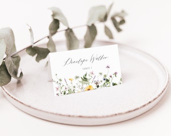 May include: White wedding place card with a floral design featuring yellow, purple, and pink flowers. The card reads "Penelope Walker, Table 1."