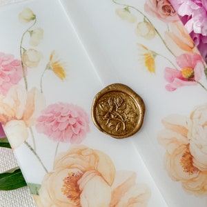 May include: A white envelope with a floral design and a gold wax seal. The flowers are pink, yellow, and white. The seal has a floral design.