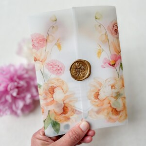 Op de afbeelding: Een witte envelop met een bloemenontwerp in tinten roze, perzik en groen. De envelop heeft een gouden waszegel met een bloemenontwerp.