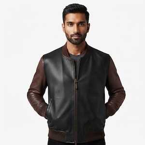 Peut inclure: Un blouson aviateur avec un panneau avant en cuir noir, des manches en cuir marron et un col, des poignets et un ourlet côtelés marron foncé. La veste présente une fermeture éclair verticale centrale et se porte sur un t-shirt gris foncé.