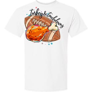 May include: A white short-sleeved t-shirt featuring a graphic print of a brown American football and a roasted turkey leg. The text "Turkey & touchdowns" is written in black cursive script above the football and turkey leg illustration.