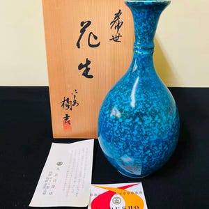 Peut inclure: Un vase en céramique bleu vif avec une texture mouchetée, doté d'un col étroit et d'un corps bulbeux. Il est accompagné d'une boîte de rangement en bois clair avec une calligraphie japonaise noire, une petite fiche d'information et une étiquette Marusho.