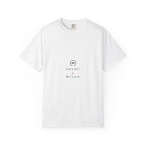 May include: A white short-sleeve t-shirt featuring a black pause symbol icon centered on the chest. Below the icon, the text reads "Can't start" followed by a red not-equal sign and the text "Don't care." The shirt has a crew neckline.