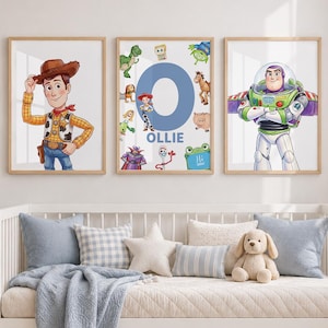 May include: Three framed wall art prints featuring Toy Story characters. The left print shows Woody, the right shows Buzz Lightyear, and the centre print features a large blue letter O with the name Ollie and various movie characters.