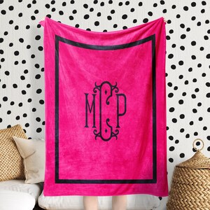 May include: A pink fleece throw blanket with a black border and a monogram of the letters "M C P" in a decorative font.