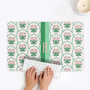 May include: A rectangular desk mat with a floral pattern in pink and green. A green stripe with the letter "H" is on the left side. A white keyboard is in the center.