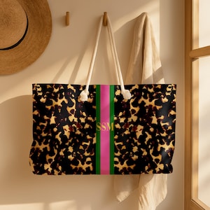 May include: A large tote bag with a tortoiseshell pattern, a pink and green stripe, and white rope handles. The bag has the initials "SSM" in gold lettering. The bag is hanging on a wall.
