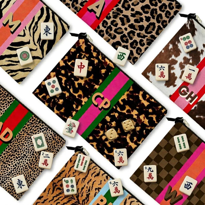 May include: An assortment of zippered pouches with various patterns, including leopard print, zebra stripes, and cowhide. Each pouch features a different design, with Mahjong tiles and initial letters. The pouches are in various colors, including pink, green, and orange.