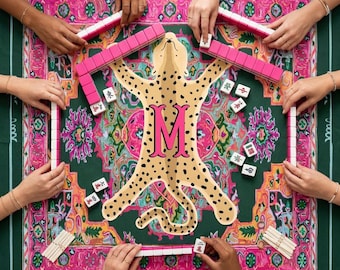 May include: A square mahjong mat featuring a central tan leopard illustration with a large pink letter M, surrounded by a vibrant pink and green floral border. The mat is set with pink mahjong tiles and white tiles with red and green symbols.