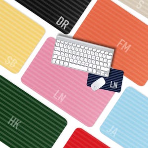 May include: A collection of personalized mouse pads and a keyboard. The mouse pads are in various colors, including pink, orange, and green, with vertical striped patterns. Each pad has initials printed on it. A white keyboard and mouse are on top of a pink mouse pad.