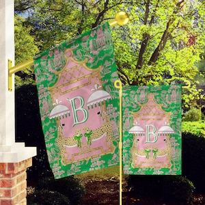 May include: Two green garden flags with a pink and gold pagoda design. The flags feature a large pink letter "B" and two leopards with pink bows. The smaller flag is on the right and the larger flag is on the left.