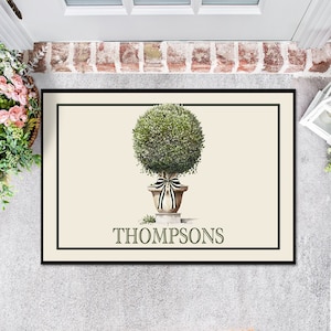 May include: A cream-colored doormat with a black border features a green topiary in a white pot with a black and white ribbon. The text "THOMPSONS" is printed in black below the topiary.