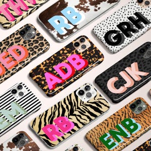 May include: A collection of phone cases with various animal print designs, including leopard, zebra, and cowhide patterns. Each case features bold, colorful initials in a block letter style, creating a personalized and stylish accessory.