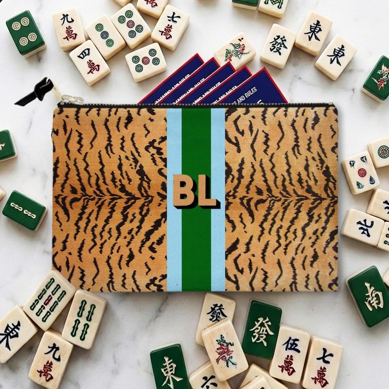 May include: A rectangular zippered pouch with a tiger stripe pattern, a central green stripe, and the initials "BL". The pouch is surrounded by Mahjong tiles, some green and some white, with Chinese characters.