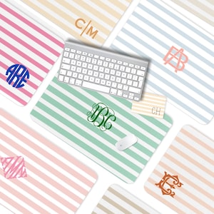 May include: A collection of personalized mouse pads with a striped design in various pastel colors, including pink, blue, and green. Each pad features a monogram in a contrasting color, with a wireless keyboard and mouse on one.