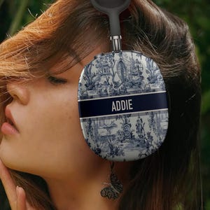 May include: Blue and white patterned headphones with the name "ADDIE" printed on the side. The headphones have a black headband and a butterfly charm hanging from the bottom.