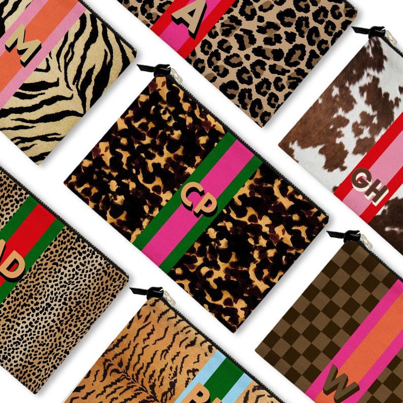 May include: A collection of zippered pouches with various animal print patterns, including zebra, leopard, and cowhide. Each pouch features a contrasting stripe and a letter or monogram in gold. The pouches are arranged on a white background.