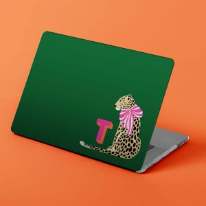 May include: A green laptop skin featuring a leopard illustration with a pink and white striped bow and a pink and orange letter "T". The leopard has black spots and is sitting down.