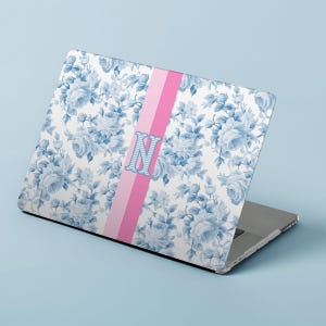 Könnte beinhalten: Laptop-Hülle mit blauem Blumenmuster auf weißem Hintergrund. Ein vertikaler rosa Streifen mit dem hellblauen Buchstaben "N" in der Mitte. Der Laptop ist abgewinkelt und zeigt das Design auf dem Deckel.