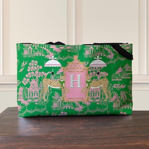 May include: Green tote bag with a pink and white Asian-inspired pattern. The design includes pagodas, flowers, and cheetahs. A pink frame with the letter "H" is centered on the bag. Black handles are visible.