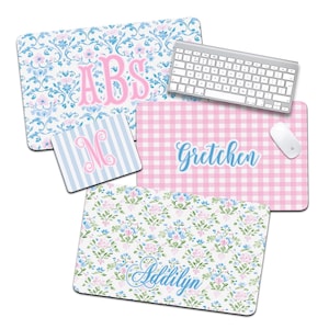 May include: A collection of personalized mouse pads and a coaster. The mouse pads feature floral, gingham, and striped patterns in pink and blue. One mouse pad has the initials "ABS", another has the name "Gretchen", and another has the name "Addilyn". A keyboard and mouse are also present.