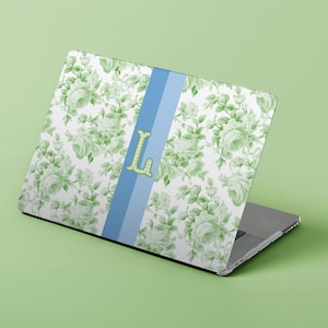 May include: Laptop with a floral design in shades of green and white. A light blue stripe runs down the center, with a green letter "L" in the middle. The laptop is open, displaying the design.