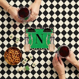 May include: A table setting with a black and white checkered pattern. The centerpiece features a green square with the letter "N" and illustrations of cheetahs holding umbrellas. Wine glasses and a bowl of pretzels are also present.