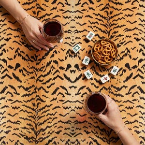 May include: Overhead shot of a table setting with two glasses of red wine, a small bowl of pretzels, and several Mahjong tiles. The table has a tiger stripe pattern in shades of orange and black.