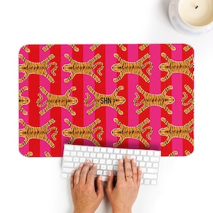 May include: A rectangular mousepad with a repeating pattern of orange tigers on a red and pink striped background. The mousepad has the letters "SHN" in the center. A white keyboard and a lit candle are also visible.