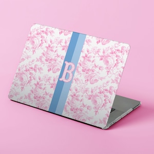 May include: Laptop with a floral pattern in pink and white, featuring a light blue stripe down the center. A pink letter "B" is centered on the blue stripe. The laptop is open, displaying the design on its surface.