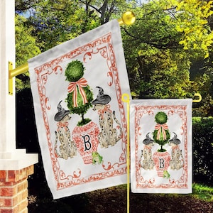 May include: Two white garden flags with a red and white topiary tree, two black cats wearing witch hats, and a frog. The flags have a red and white border with a decorative scroll design. The larger flag has the letter "B" in the center of the topiary tree. The smaller flag has the letter "B" in the center of the topiary tree.