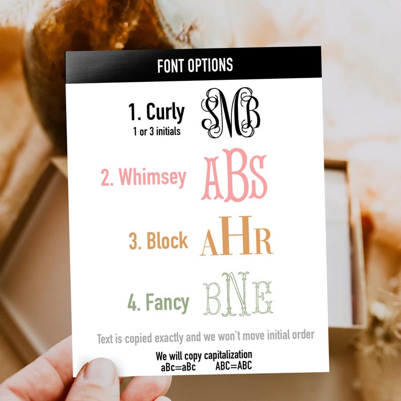May include: A white rectangular card titled FONT OPTIONS displaying four styles: 1. Curly with black script initials, 2. Whimsey with pink serif initials, 3. Block with orange serif initials, and 4. Fancy with green outlined initials, plus text instructions.