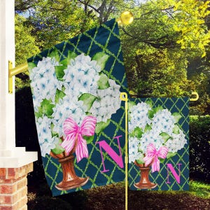 May include: Two garden flags with a blue background and a white lattice pattern. The flags feature a watercolor illustration of a bouquet of white hydrangeas with a pink bow and a letter N.