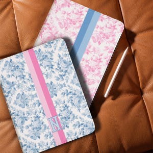 May include: Two floral-patterned tablet cases. One case features a pink and blue floral design with a pink stripe. The other case has a pink floral design with a blue stripe. A white stylus is also visible.