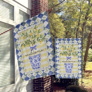 May include: Two welcome garden flags with a blue and white checkered background. The flags feature a lemon tree in a blue and white planter with a yellow and white striped background. The text "welcome" is written on each flag.