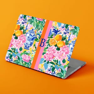 May include: A laptop skin featuring a vibrant floral and citrus pattern with blue and white ginger jars, pink hydrangea blossoms, and orange fruit. A vertical orange and pink stripe runs down the center, displaying a large blue letter B.