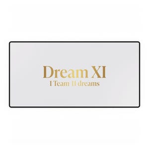 May include: A rectangular desk mat with a white surface and a thin black border. The centre features the gold text "Dream XI" in a large serif font, with the smaller gold text "1 Team 11 dreams" positioned directly underneath it.
