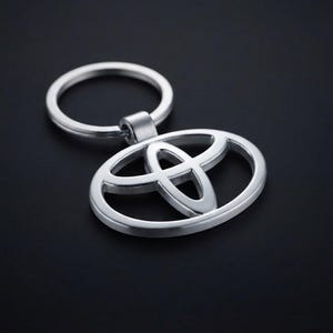 May include: A silver-toned metal keychain featuring the Toyota logo, which consists of three overlapping ellipses. The keychain includes a circular split ring attached to the top of the emblem, showcasing a smooth, polished finish throughout.